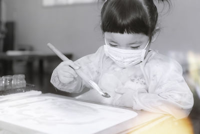 Girl painting while sitting by table at home