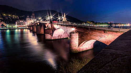 Illuminated bridge over river against sky in city at night