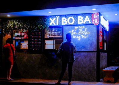 Rear view of man standing at illuminated store