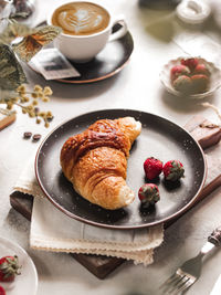 Fresh baked croissant with strawberry fruits in ceramic black plate