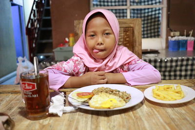 Girl wearing hijab sticking out tongue while having meal at home