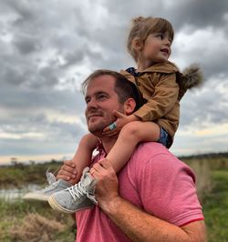 Father carrying daughter against sky
