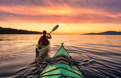 Man in sea against sky during sunset