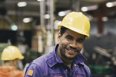 Portrait of confident male blue-collar worker wearing hardhat in factory