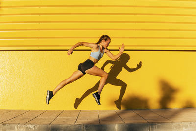 Side view of woman jumping against yellow wall