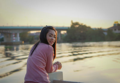 Portrait of young woman standing against lake during sunset