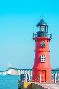 Lighthouse by sea against clear blue sky