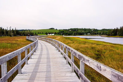 Boardwalk amidst grassy field against sky