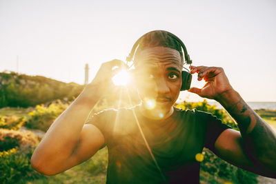 Young man adjusting wireless headphones on sunny day