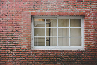 Old red brick wall texture background with classic white wooden frame and sash window with glass