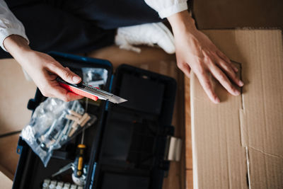 Midsection of woman holding cutter over cardboard box