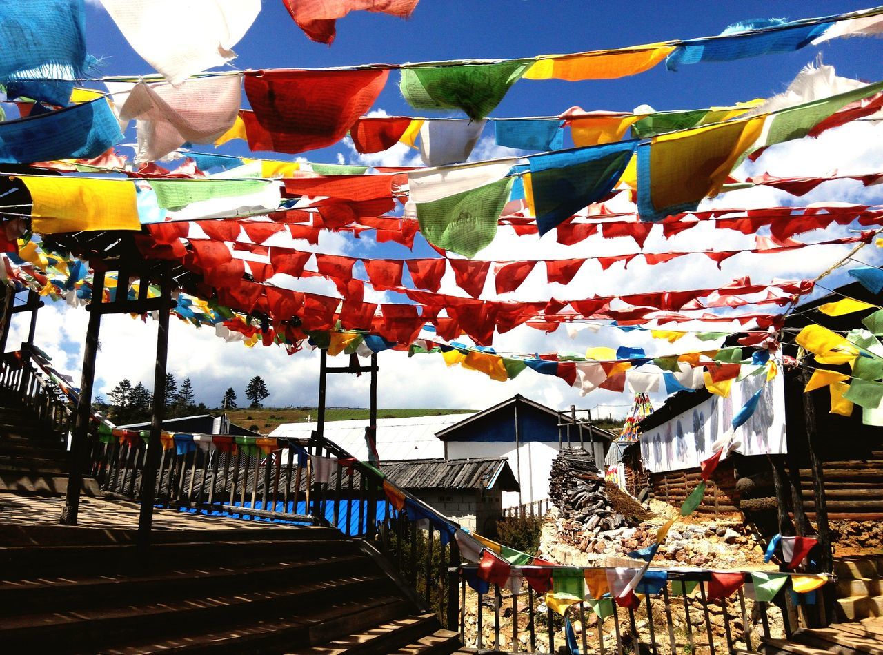 architecture, building exterior, built structure, multi colored, hanging, parasol, sky, house, residential building, in a row, flag, sunlight, day, residential structure, umbrella, roof, outdoors, colorful, drying, no people