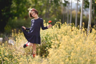 Portrait of girl with flower standing on field against trees