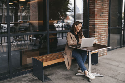 Young woman using mobile phone while sitting on seat at home