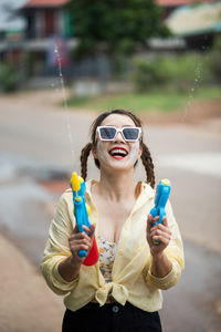 Portrait of young woman holding sunglasses while standing outdoors