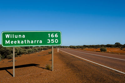 Road sign by road against clear blue sky