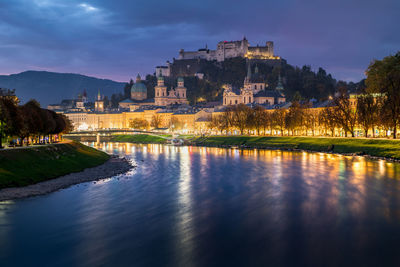 Buildings by river against sky at night