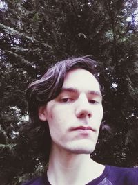 Portrait of young man looking away against trees