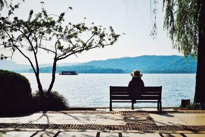 Rear view of man sitting by sea against clear sky