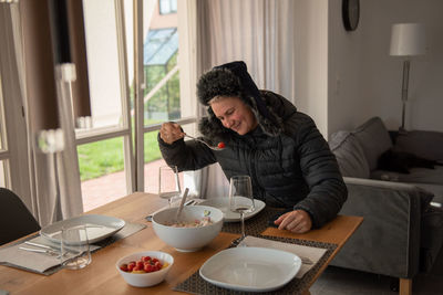 A woman sits at the dining table, dressed warmly, and eats