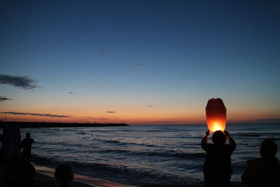 Silhouette people on beach against sky during sunset