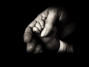 Cropped parent holding hand of baby against black background