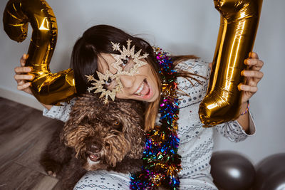 Portrait of woman wearing mask sitting with dog and balloons on floor at home