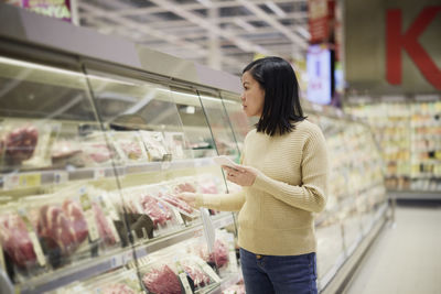 Woman doing shopping in supermarket and using cell phone to compare prices or checking shopping list