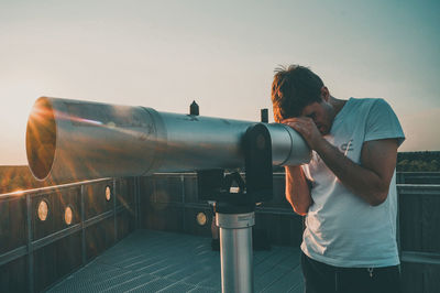 Man looking through telescope while standing against sky