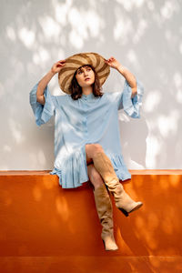 Portrait of young woman sitting against wall