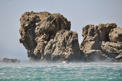 Rock formation in sea against clear sky