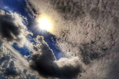 Low angle view of sun shining through clouds