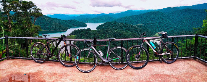 Bicycles on railing by lake against mountains