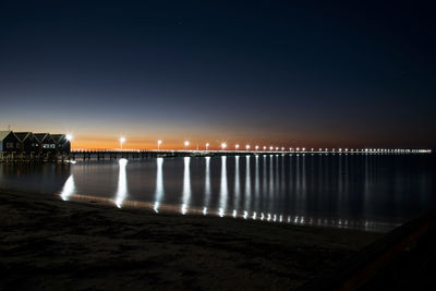 Illuminated city by river against sky at night