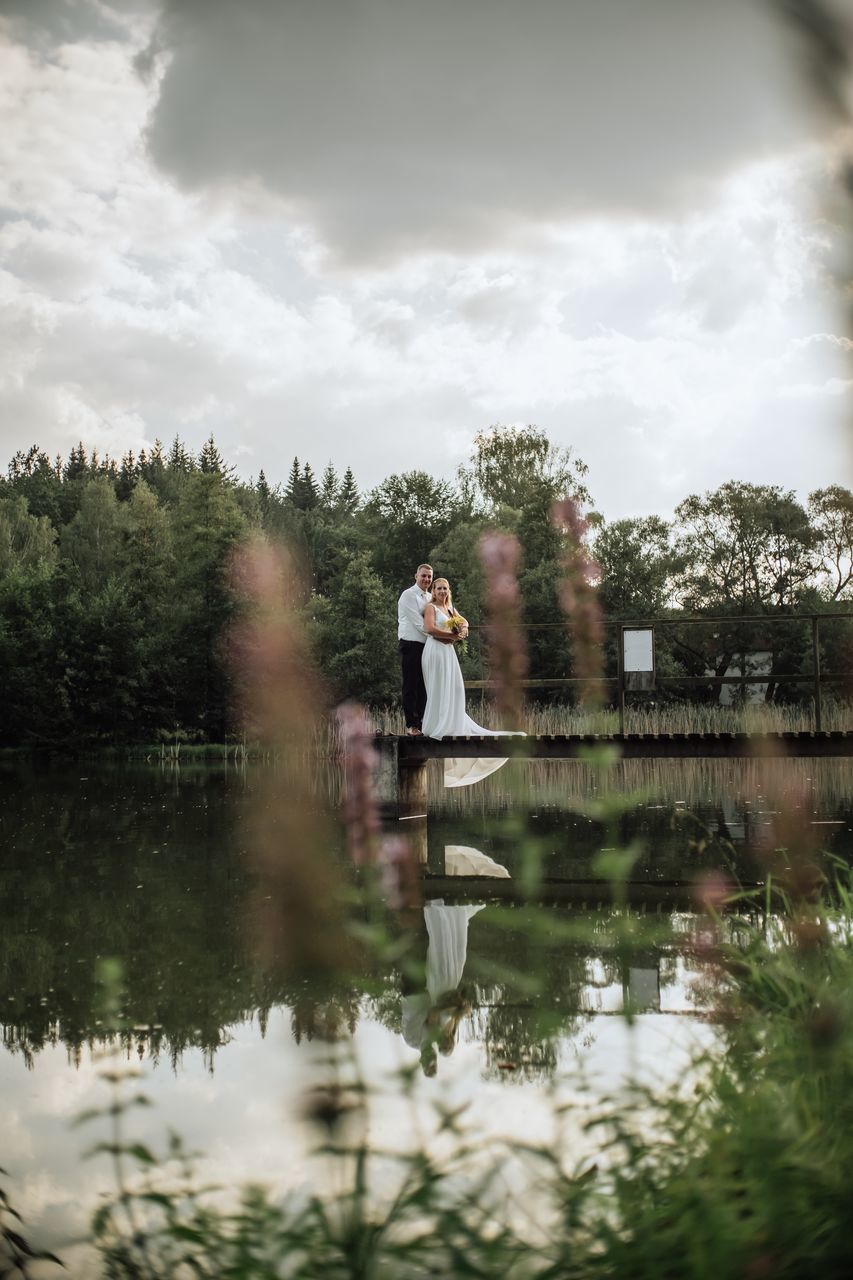 water, one person, reflection, sky, tree, standing, cloud - sky, lake, real people, plant, nature, beauty in nature, day, adult, three quarter length, lifestyles, waterfront, young adult, outdoors