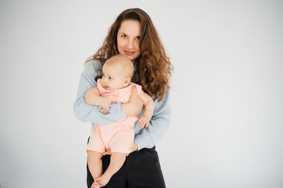 Young mother with long hair and in a shirt holds a newborn daughter. in the arms of a 6 month old 