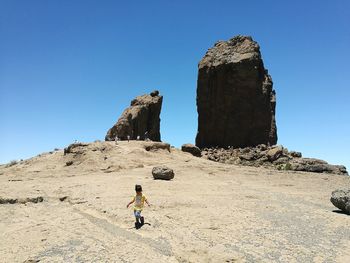 Man standing on rock formation against clear blue sky
