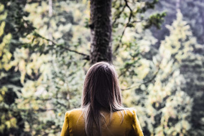 Rear view of woman standing against trees in forest