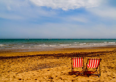 Deck chairs on beach against sky