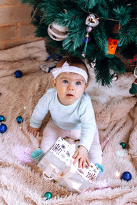 High angle view of girl with gift by christmas tree on carpet