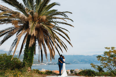 Full length of couple embracing while standing against sky