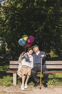 Happy senior couple with balloons sitting on bench in a park