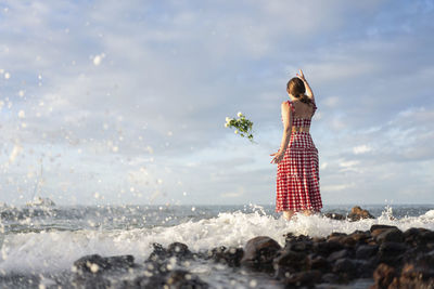 Woman standing on rock by sea against sky