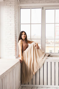 Portrait of young woman standing against window