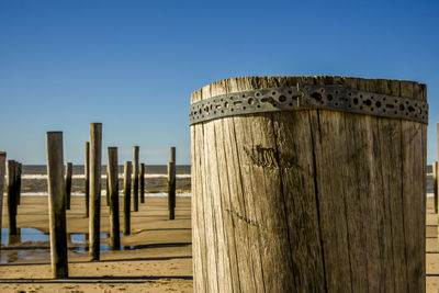 Wooden posts on beach against clear blue sky