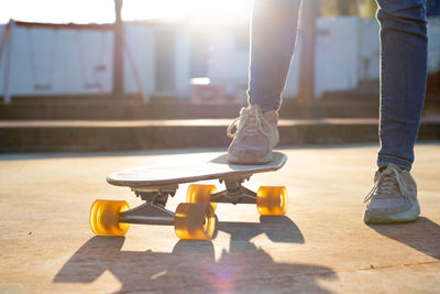 Beautiful backlit photo of a cruiser skateboard held by the feet of a young girl in the park