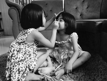 Girl applying make-up to sister sitting on rug