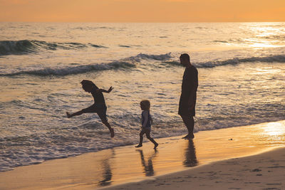 People playing at beach during sunset