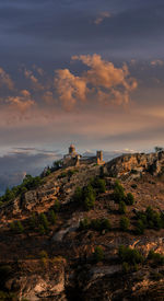 Castle on rock by building against sky during sunset