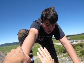 Cropped hands of people holding boy against landscape and clear sky